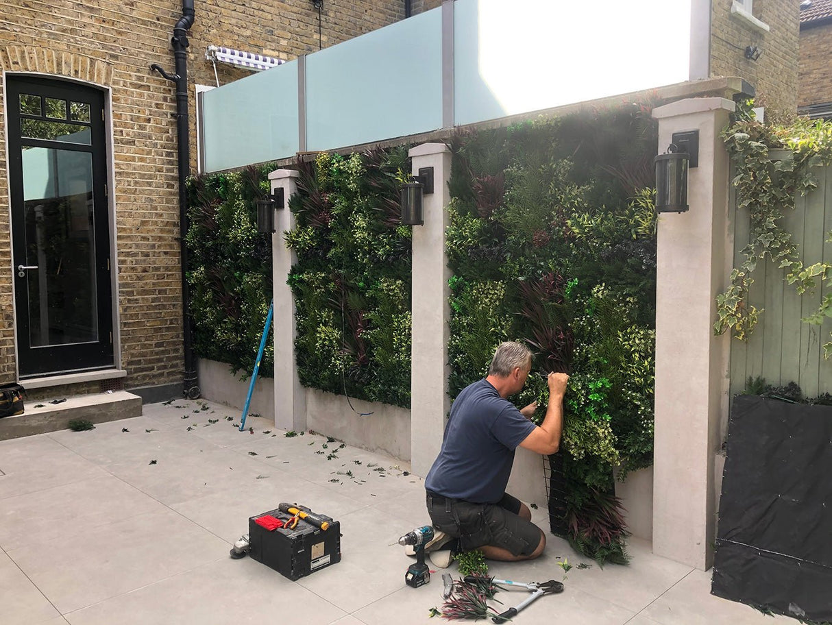 Artificial green foliage wall panel on a courtyard wall, dense mixed leaves and flowers