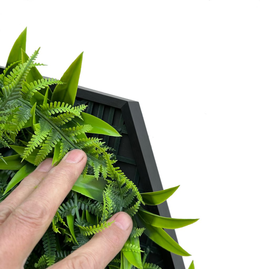 Artificial green fern leaves tucked into a hexagonal aluminium frame, close-up.