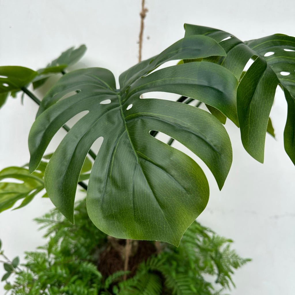 Artificial monstera-style leaf with cutout lobes on a hanging kokedama plant