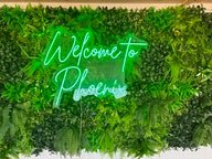 Artificial foliage wall panel with handwritten-style “Welcome to” text in green