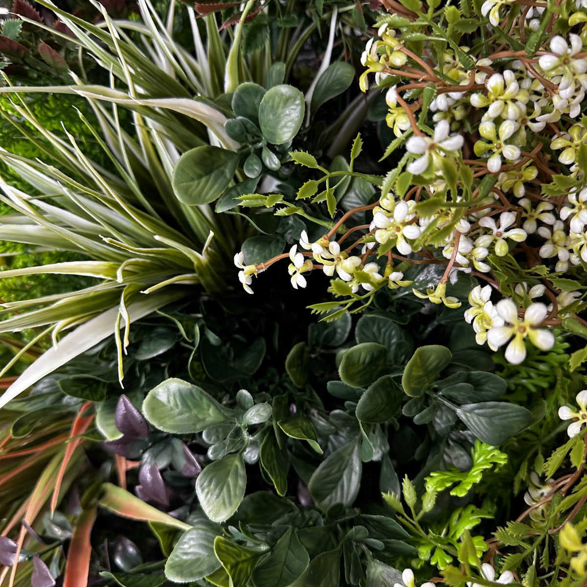 Artificial plant wall panel close-up of faux grass blades, dark leaves, and white blossoms