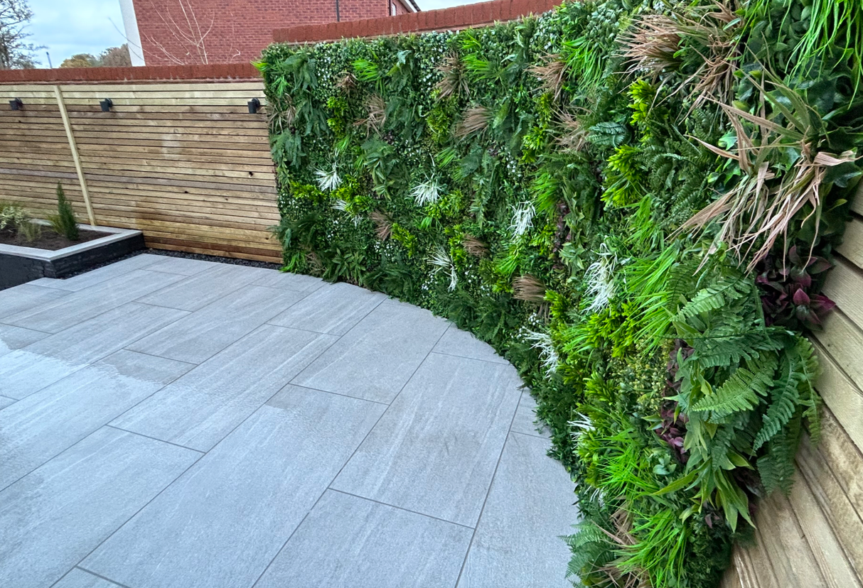 Artificial green wall panel with mixed foliage and small white flower accents along an edge
