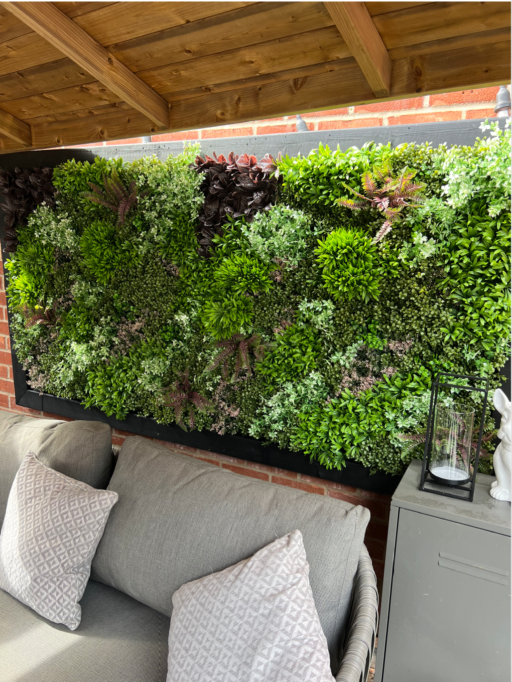 Artificial wall panel display with dense mixed foliage in greens, burgundy accents, and white tips