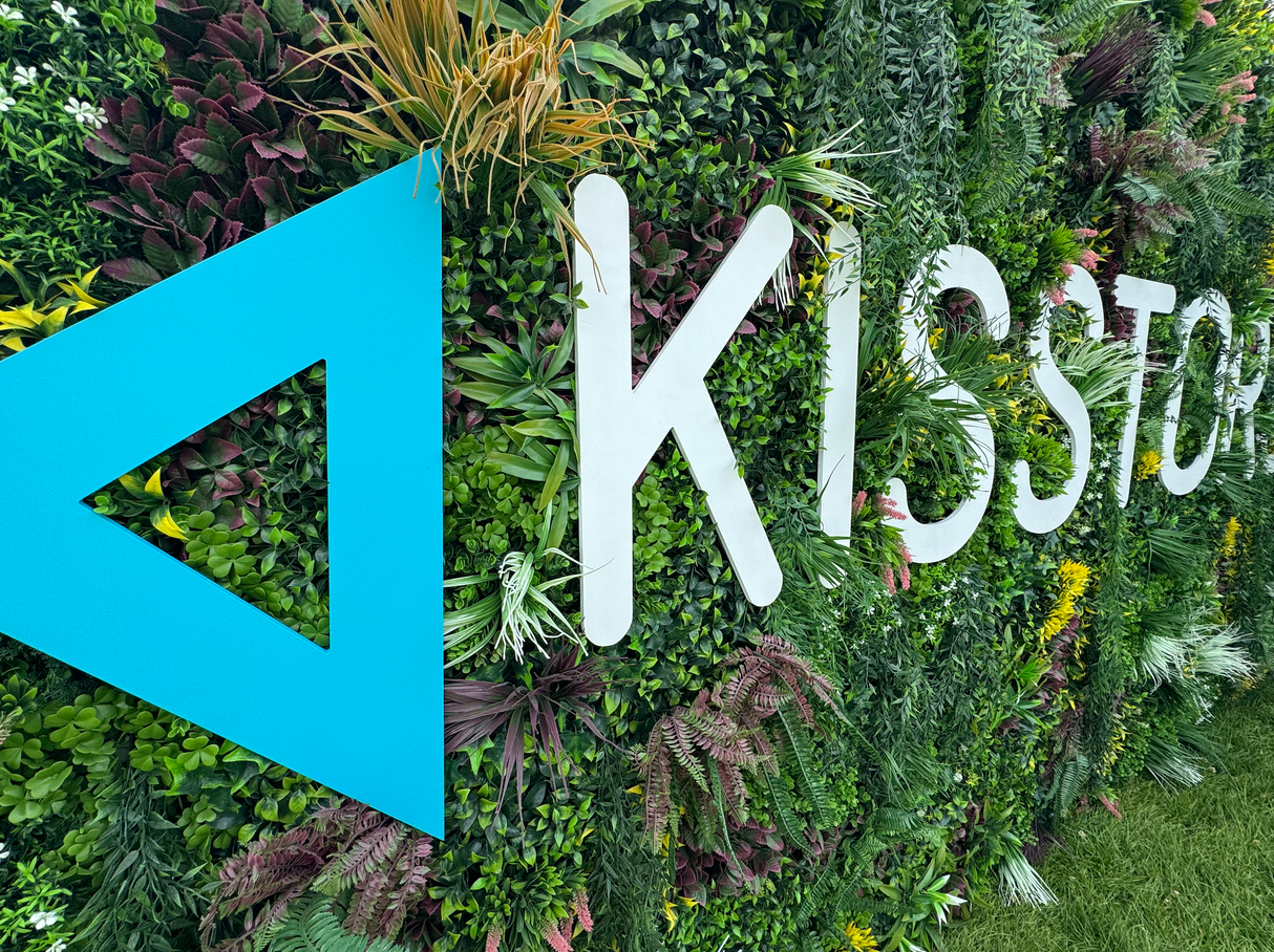 Artificial green wall panel with dense foliage and large turquoise and white cutout letters