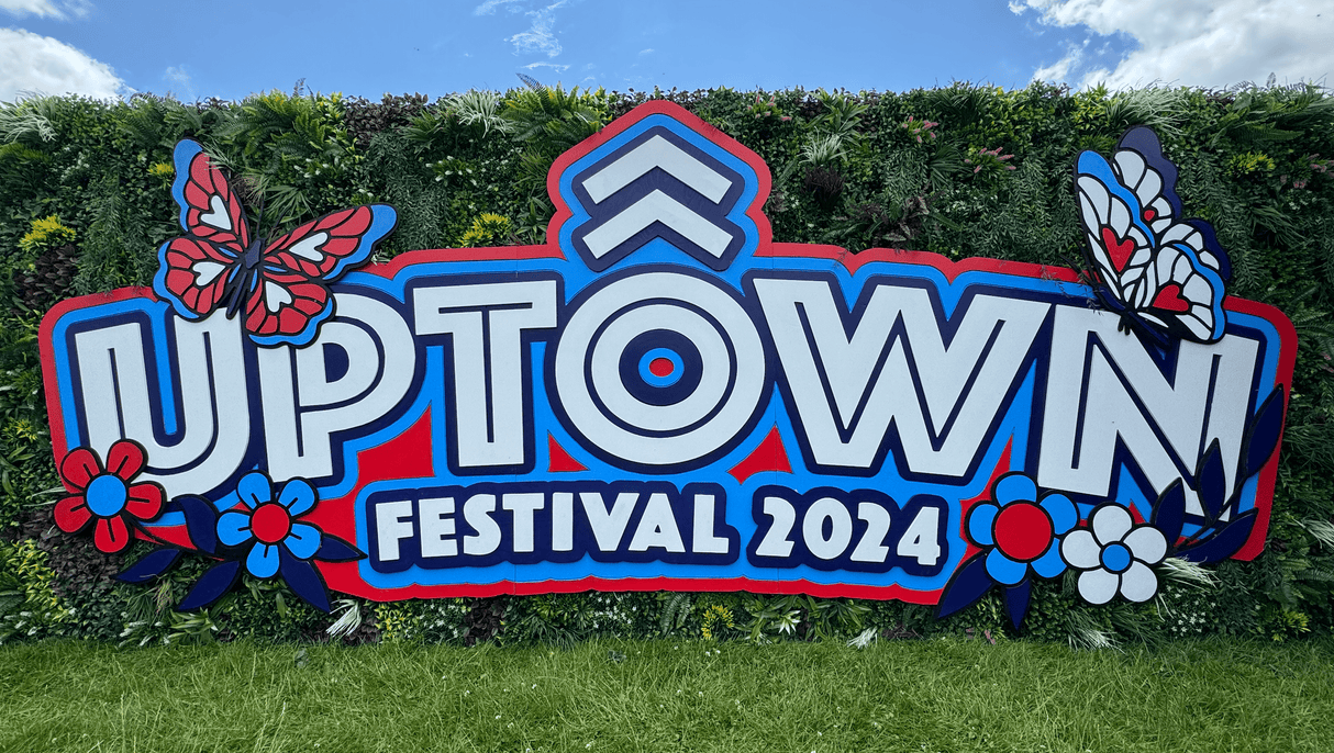 Artificial green foliage wall panels forming a hedge behind a large festival banner sign