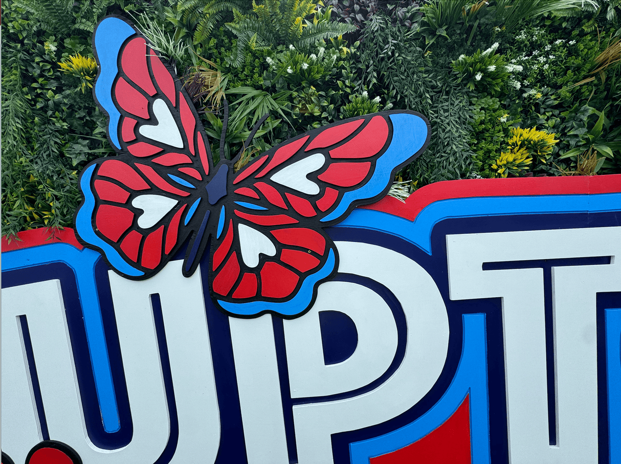 Artificial green wall panel with butterfly and large white-blue-red cutout letters