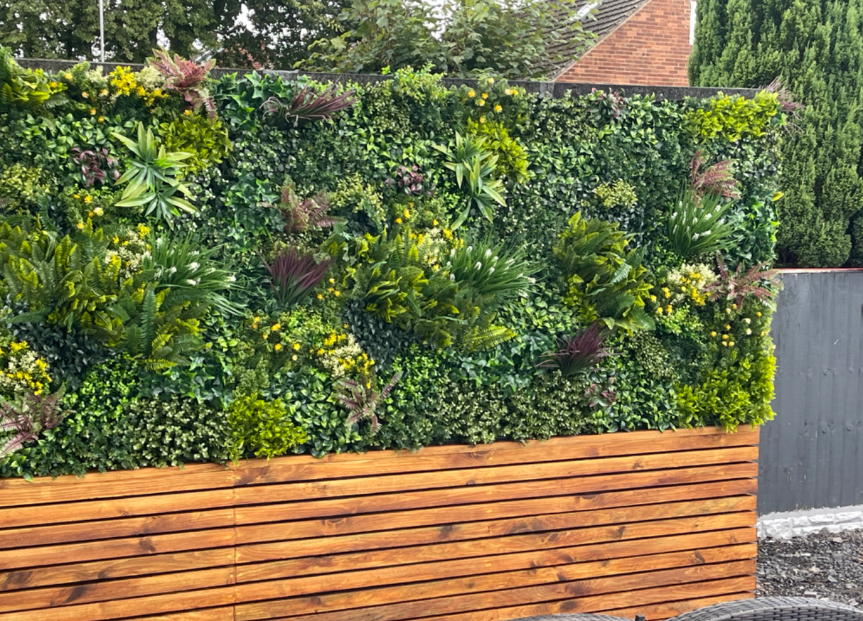 Artificial green foliage wall panel on wooden planter with yellow flower clusters and ferns