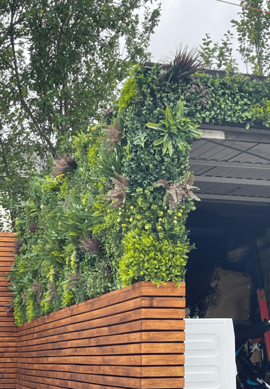 Artificial green wall panel on a planter wall with layered foliage and fern fronds