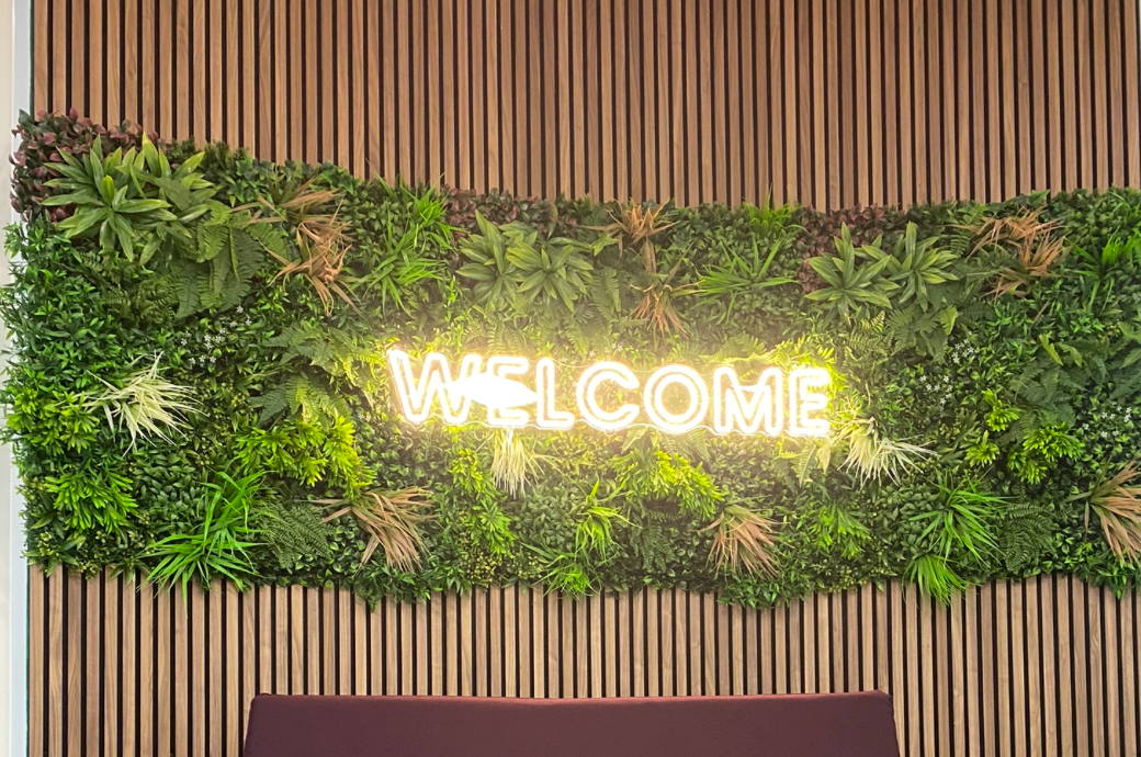 Artificial green wall panel with dense mixed greenery covering a vertical slat wall