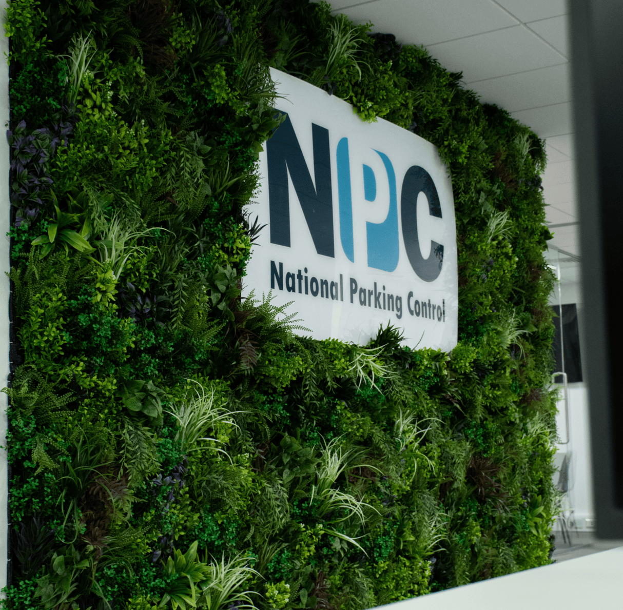 Artificial foliage wall panel with white NPC National Parking Control sign mounted