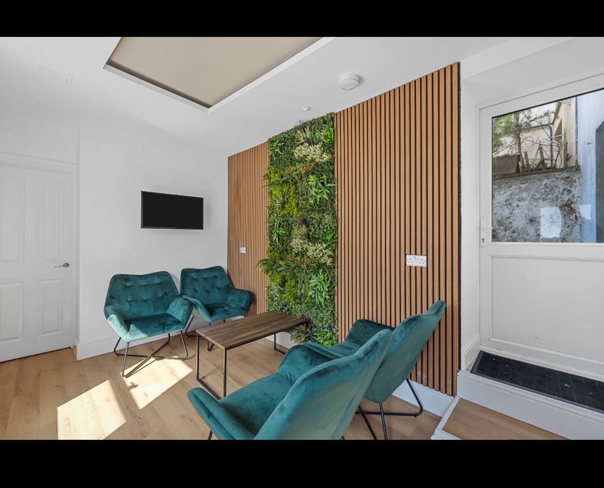 Artificial green foliage wall panel, dense mixed-leaf texture on a square wall section.