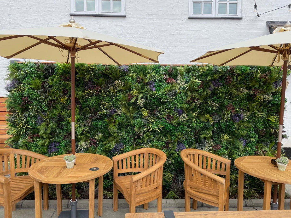 Artificial plant wall backdrop with dense green foliage and subtle purple and red accents