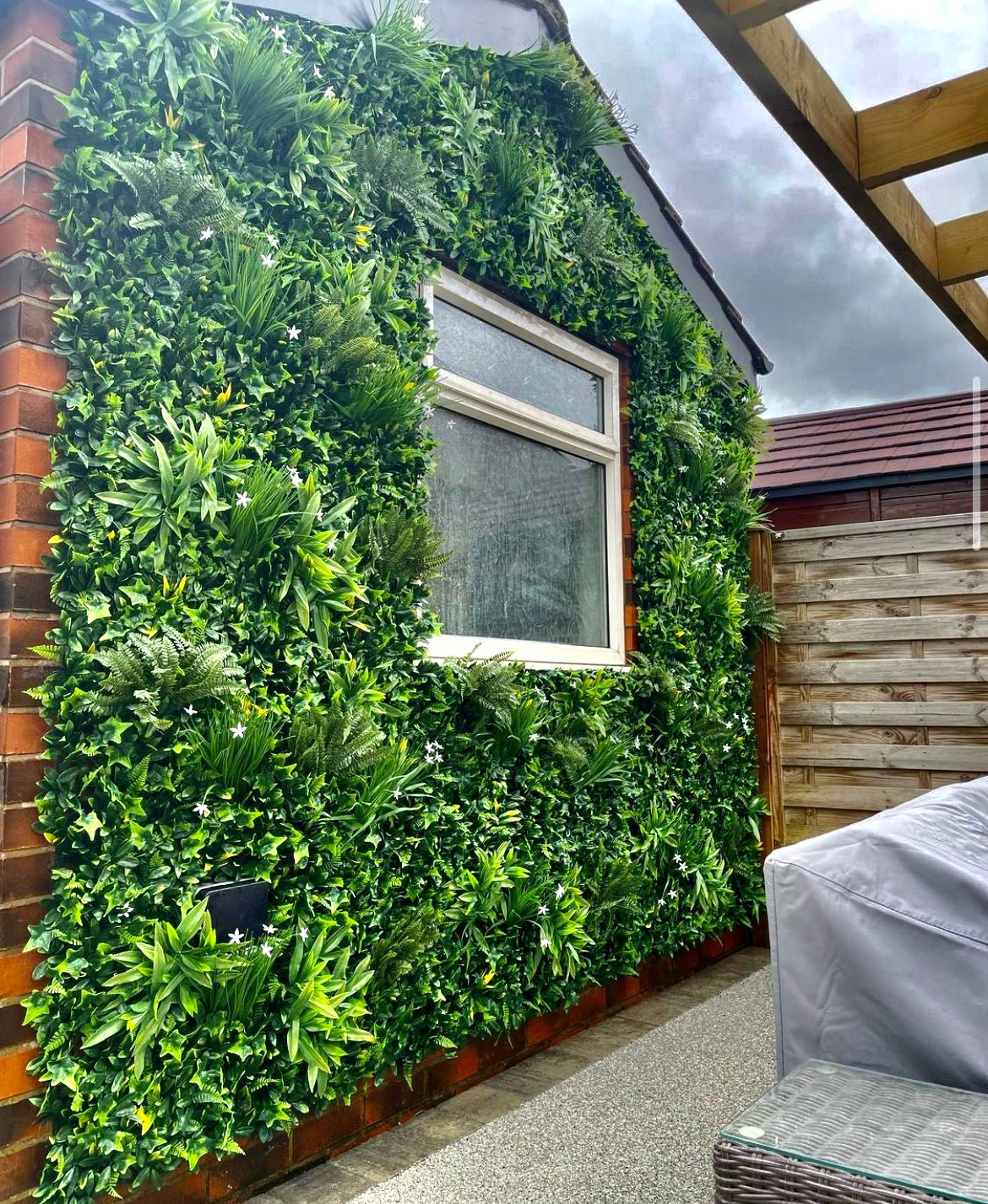 Artificial green wall panel with dense ivy, ferns and small white flowers