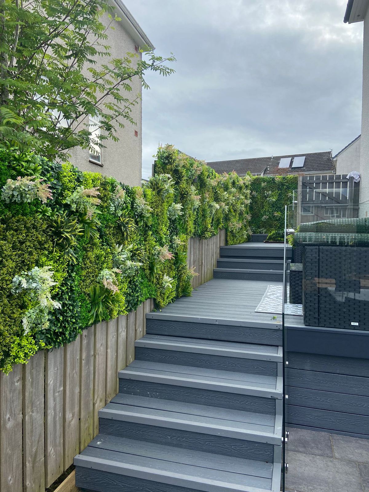 Artificial green foliage wall panel with hedge-style leaves along side steps and fence