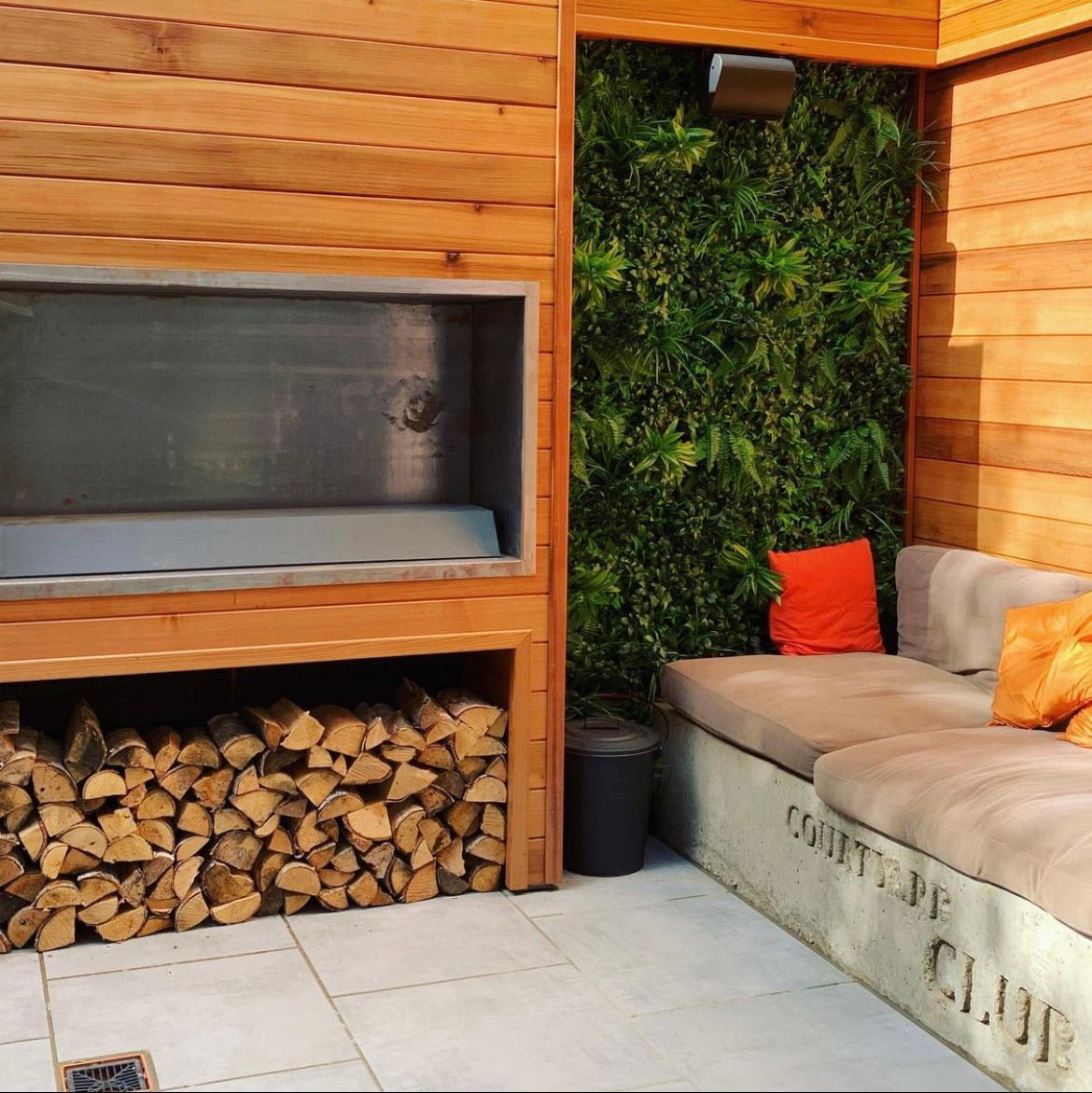 Artificial green wall panel in a patio nook with dense faux foliage behind seating