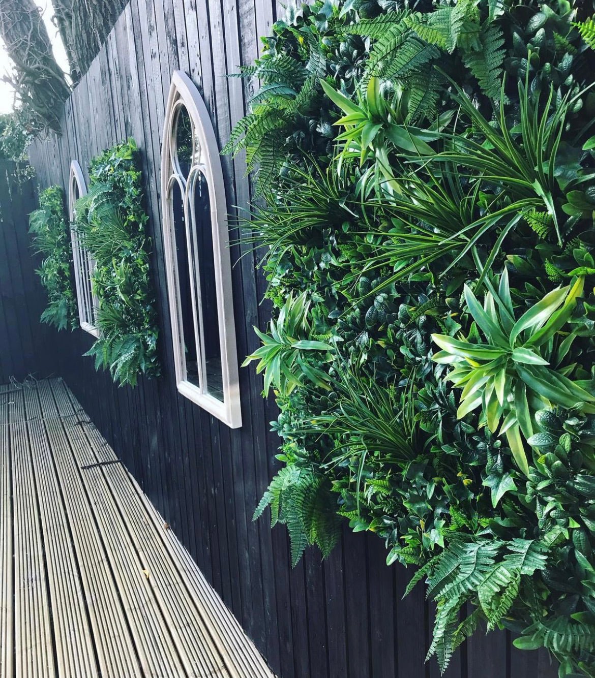 Artificial green wall panel with dense faux leaves covering an outdoor wooden wall