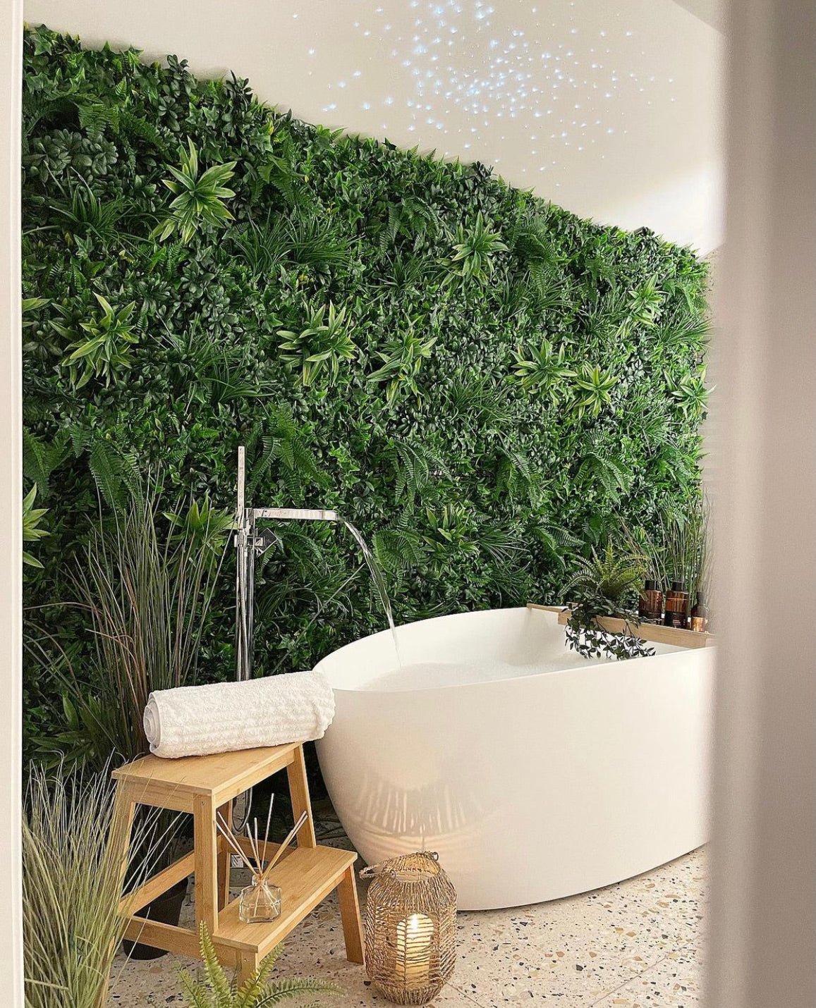 Artificial green wall panel along a bathroom corner with dense faux foliage above a bathtub
