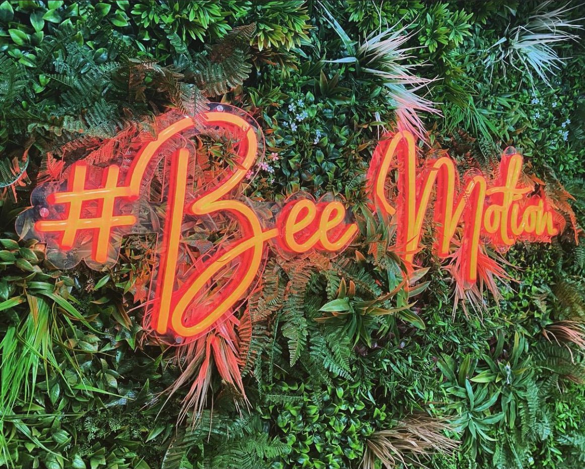 Artificial green foliage wall panel with orange neon '#Bee' graphic over leaves