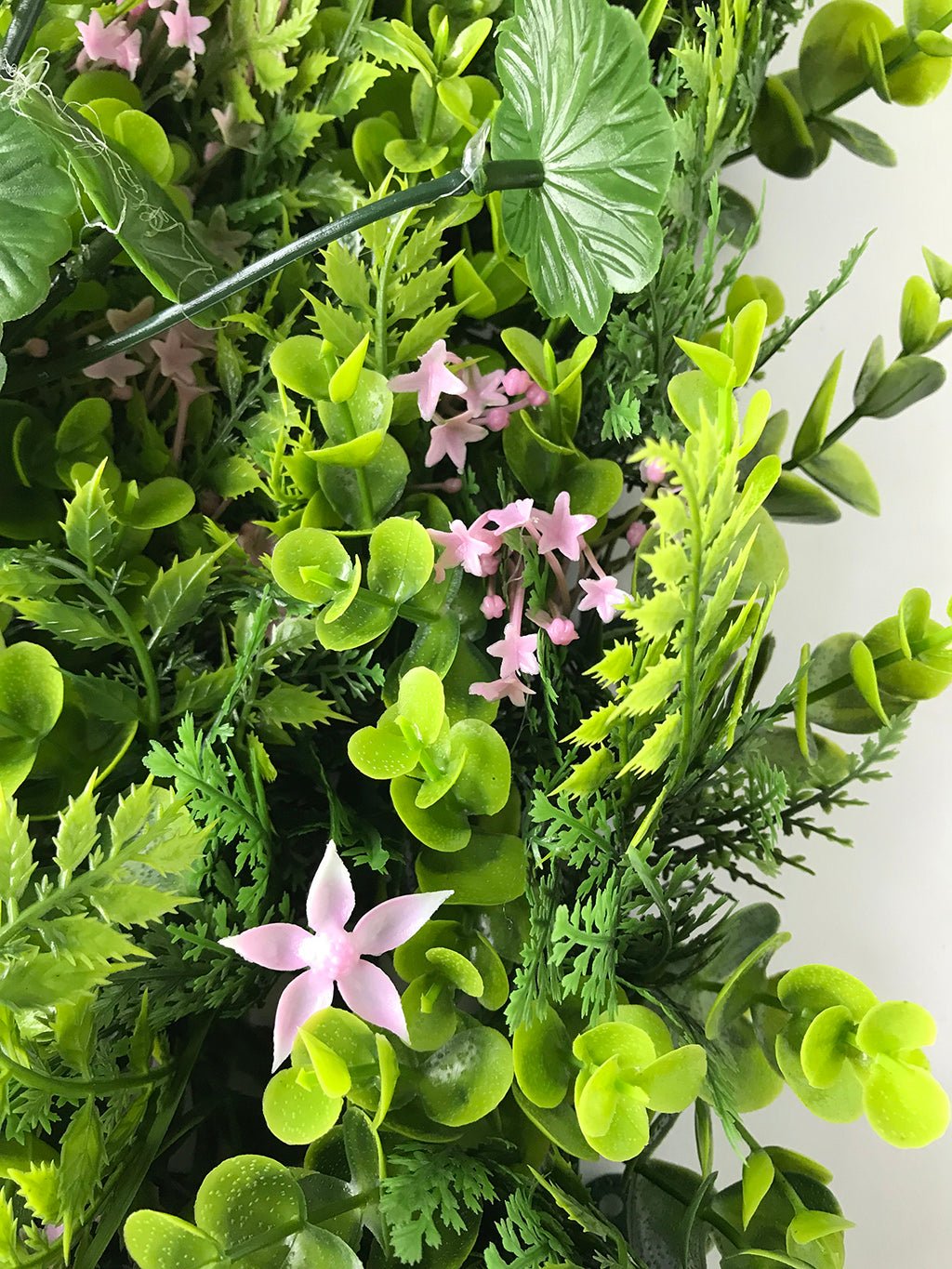 Artificial green plant wall panel with small pink star flowers among mixed foliage
