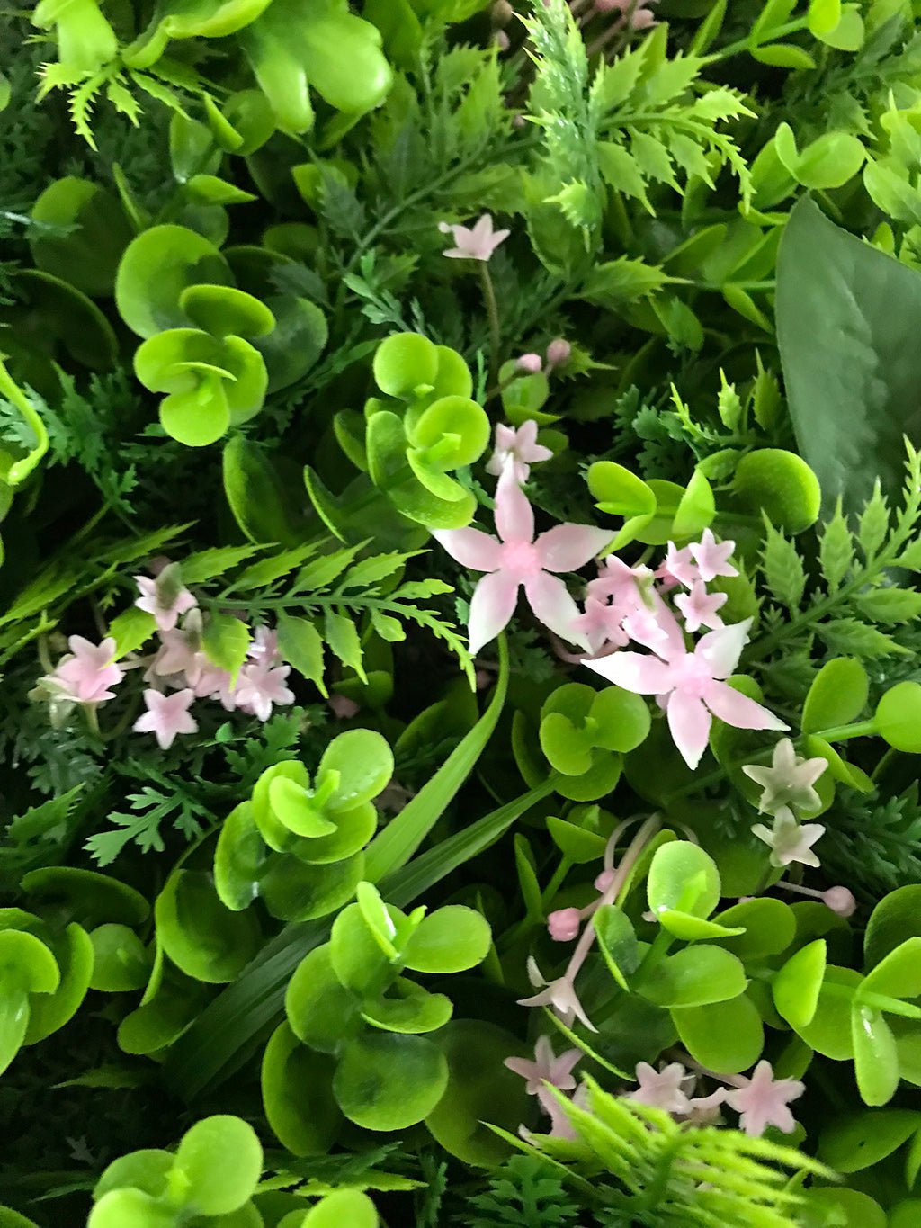 Artificial green plant wall panel with small pink flowers over fern-like and leafy greens