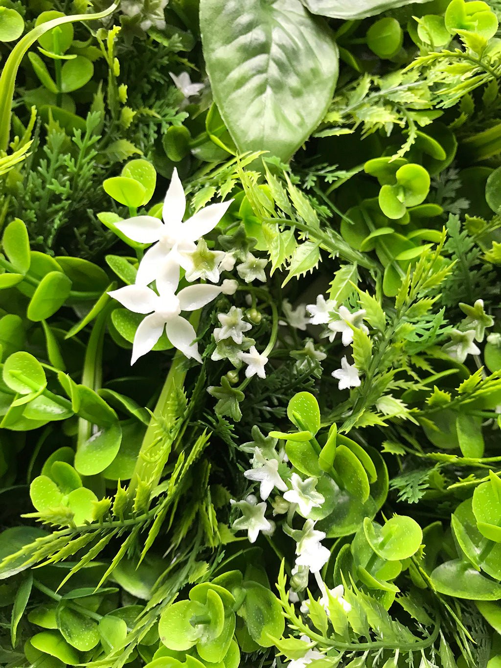 Artificial green plant wall panel with white star flowers and mixed green foliage
