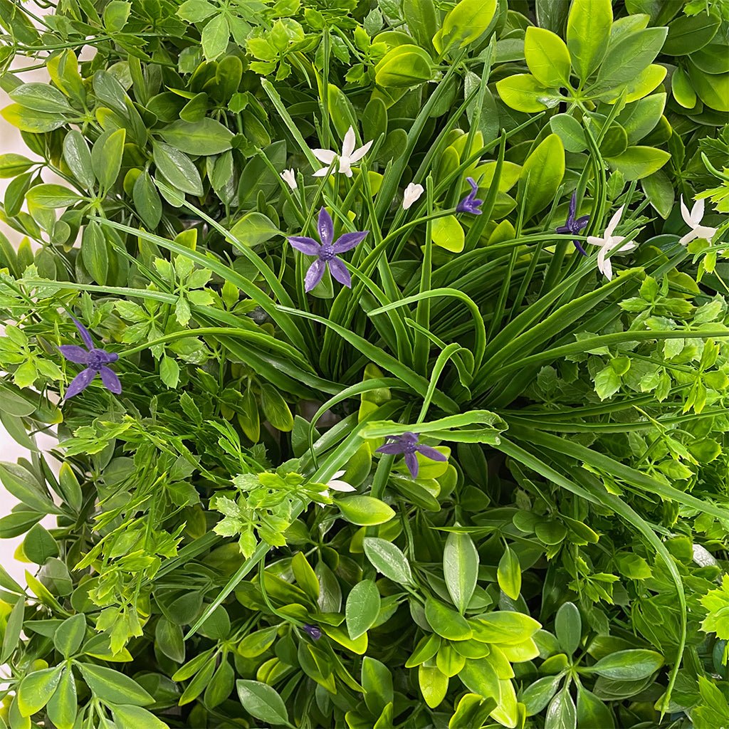 Artificial green foliage wall panel close view with purple and white star-like flowers