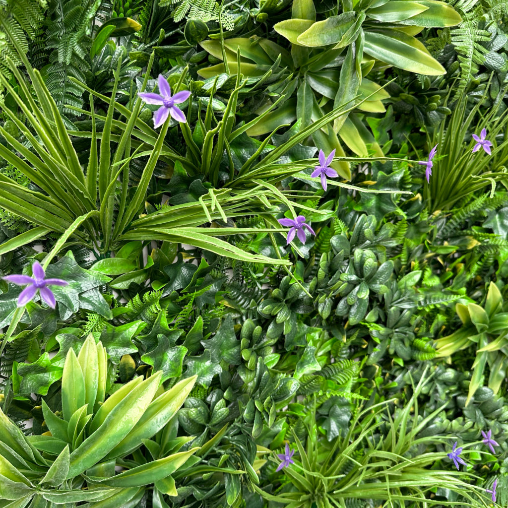 Artificial green wall panel with variegated greens of ivy, ferns, palm heads, grasses & small purple flowers 100x100 cm