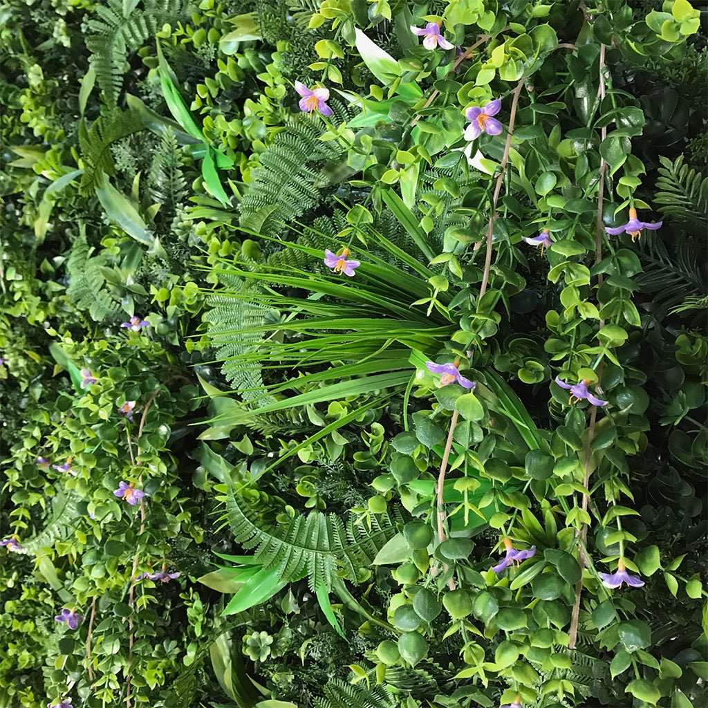 Artificial foliage wall panel close-up with green leaves and scattered purple flowers