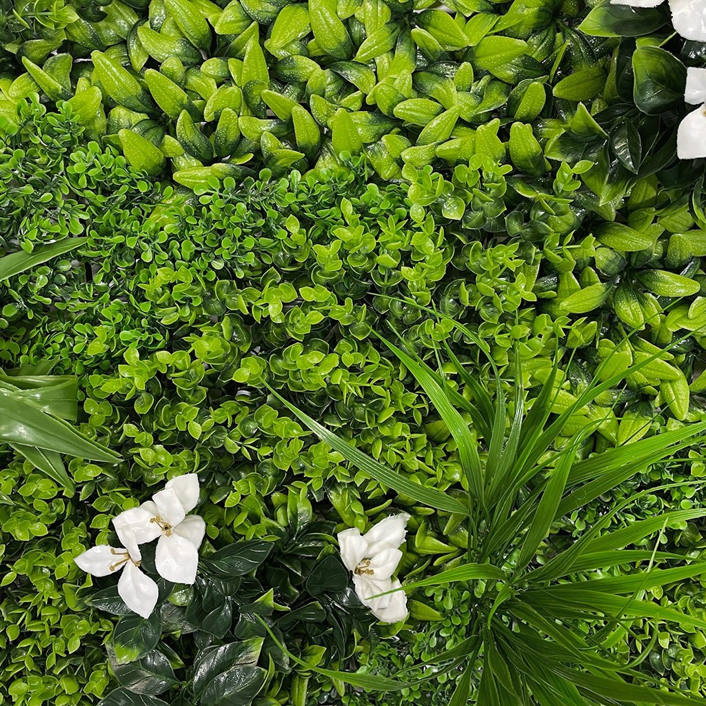 Artificial green wall panel close-up of bright green leaves, grass blades, white flowers