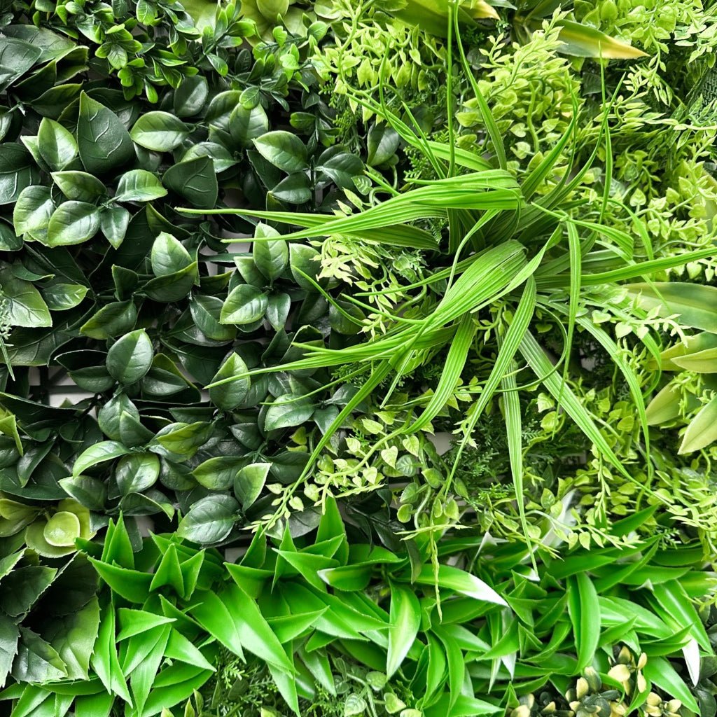 Artificial foliage wall panel detail: layered green leaves, grasslike blades, and small foliage
