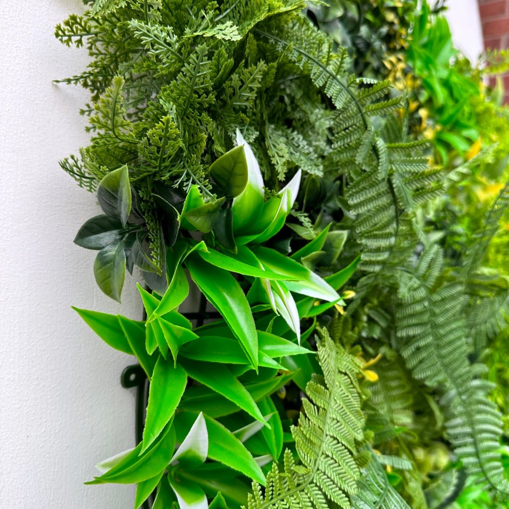 Artificial foliage wall panel corner view with bright green leaf sprigs and fern fronds