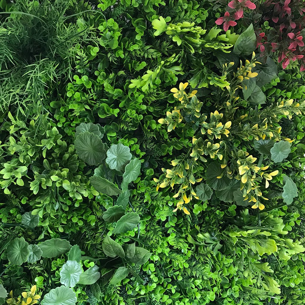 Artificial plant wall panel close-up with leafy greens, yellow highlights, and broad leaves