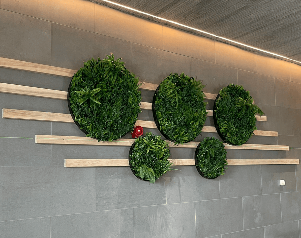 Green artificial foliage circular panels mounted on a gray stone wall