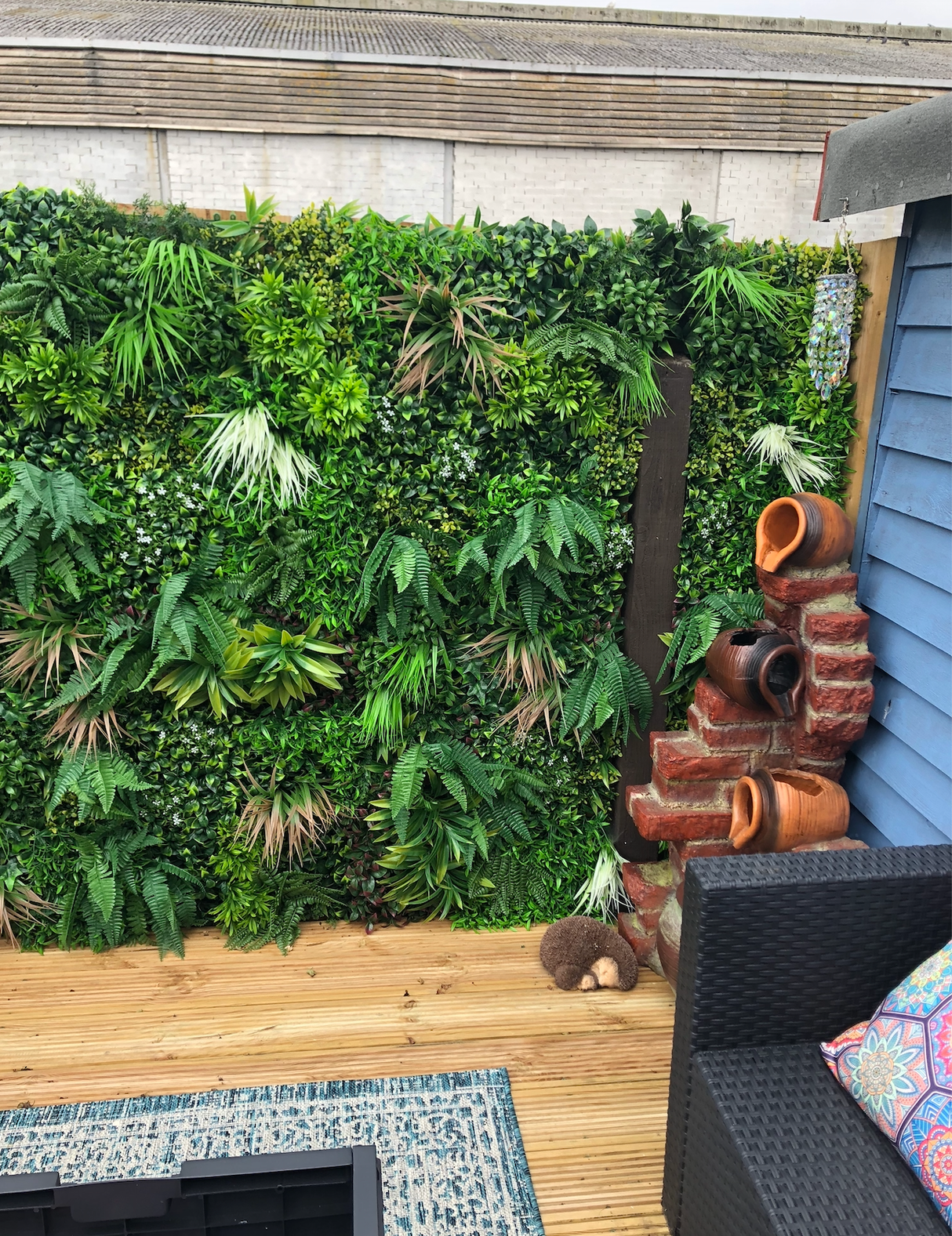 Artificial green foliage wall panel with dense leaves covering a garden fence section