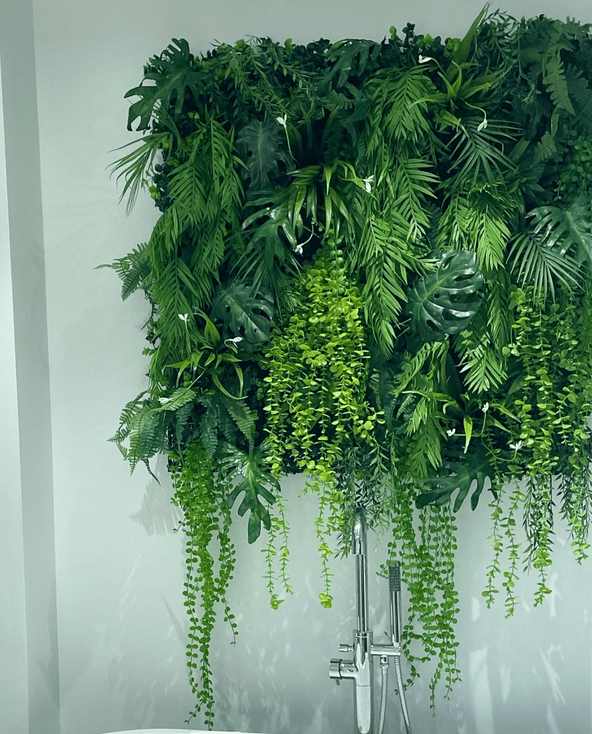 Artificial tropical plant wall with layered leaves, bright green center, and hanging vines