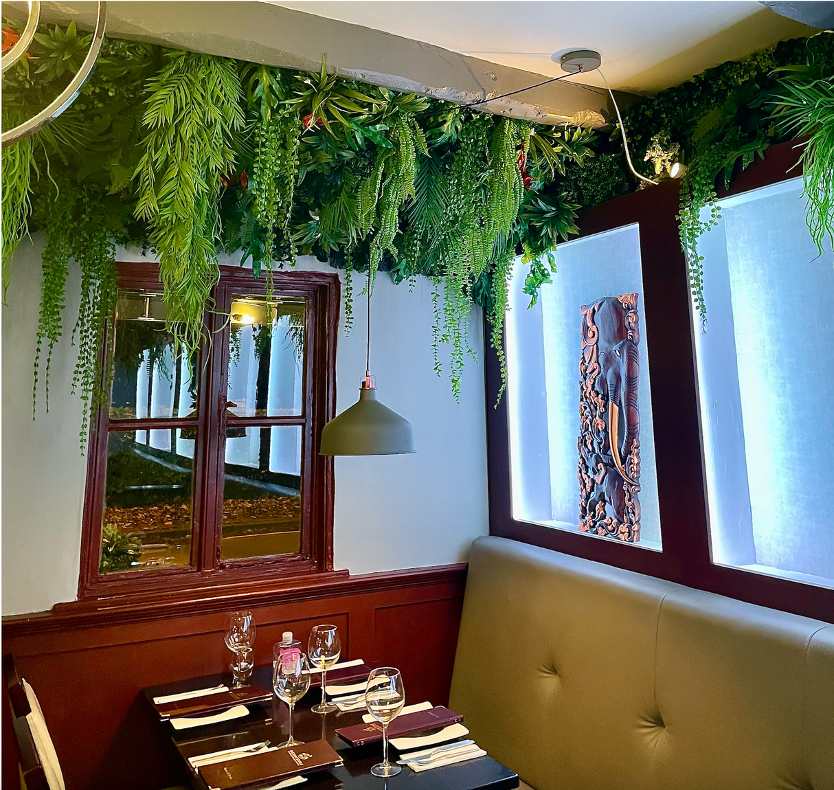 Artificial tropical plant wall with hanging green foliage over windows and a lounge seating area