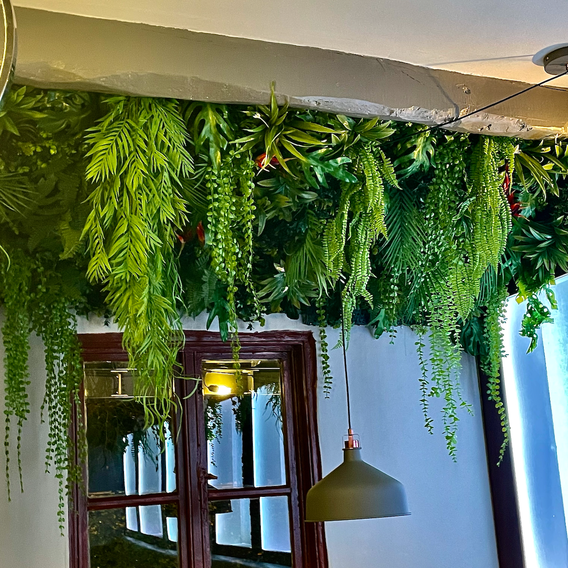 Artificial tropical plant wall installation with long trailing green vines and fern-like leaves