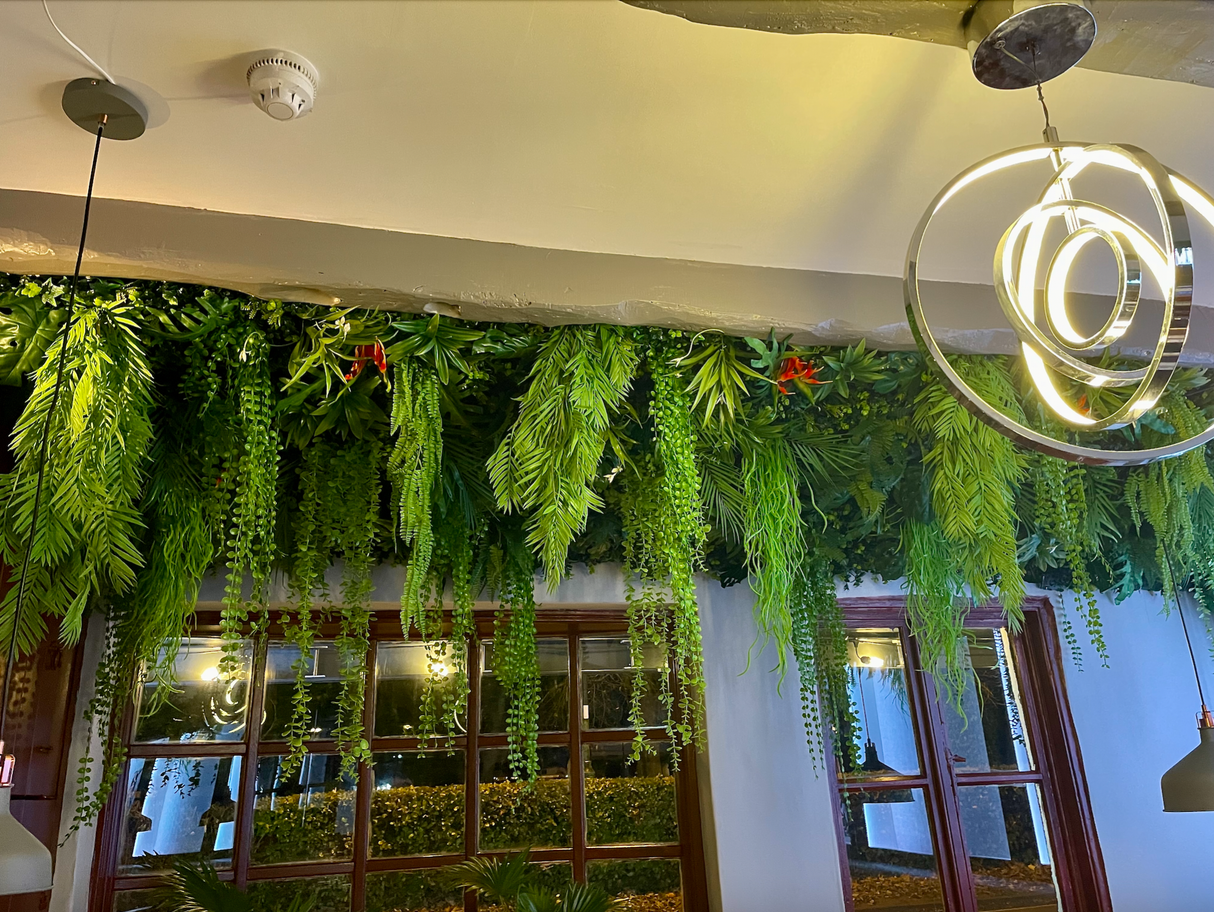 Artificial jungle plant wall installation with dense hanging green leaves along a ceiling edge