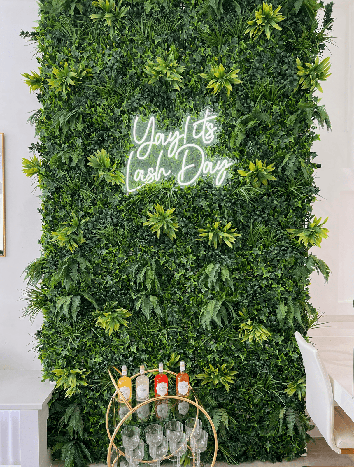 Artificial green foliage wall panel with neon script sign and dense overlapping leaves