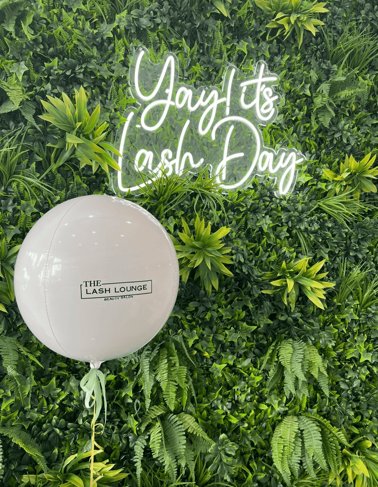 Artificial green foliage wall panel with neon script sign and lush fern-like foliage