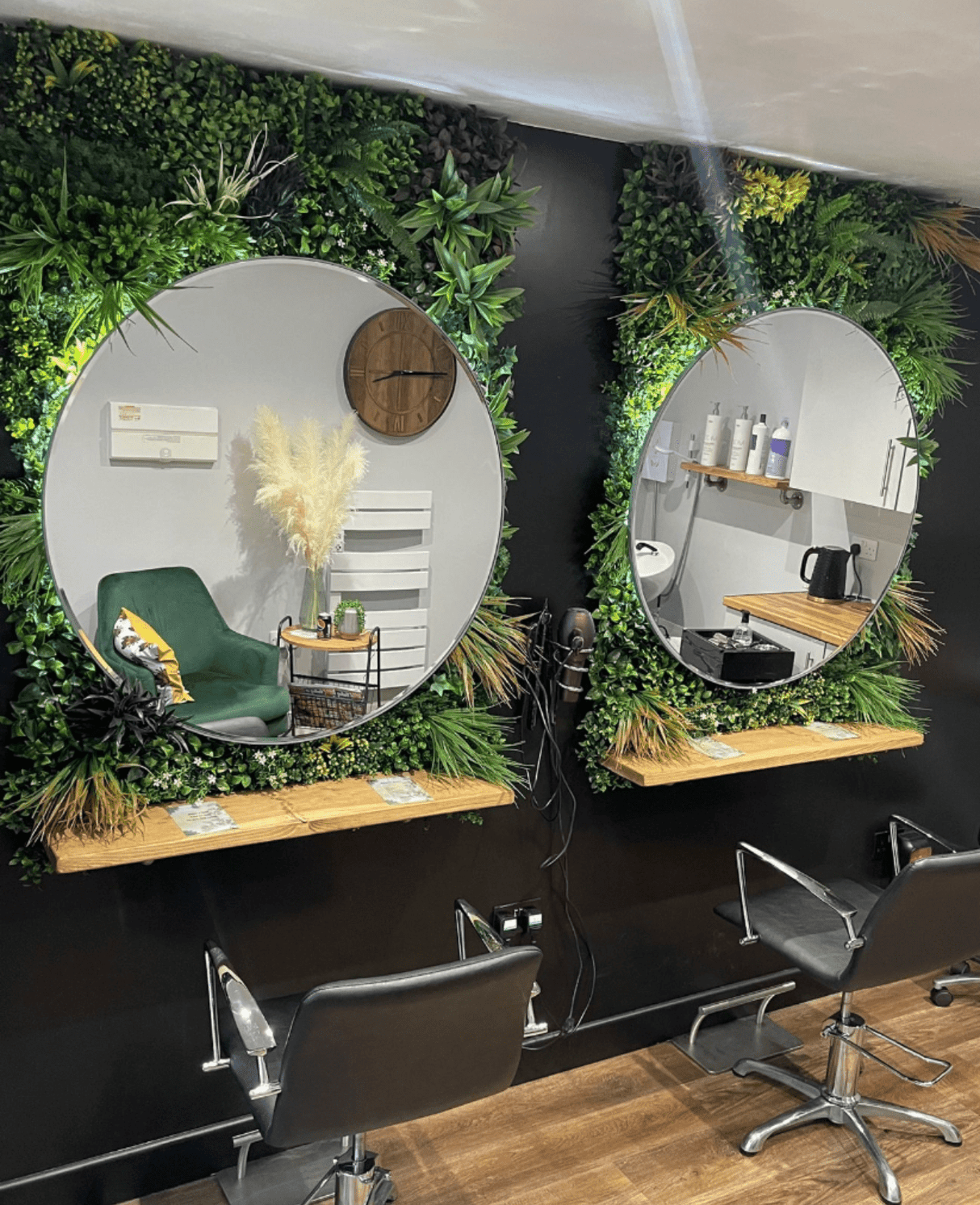 Indoor artificial foliage wall panel with dense mixed greens behind two round mirrors