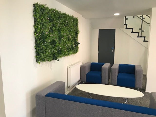 Artificial green plant wall panel mounted on wall with dense greenery and pink flower specks