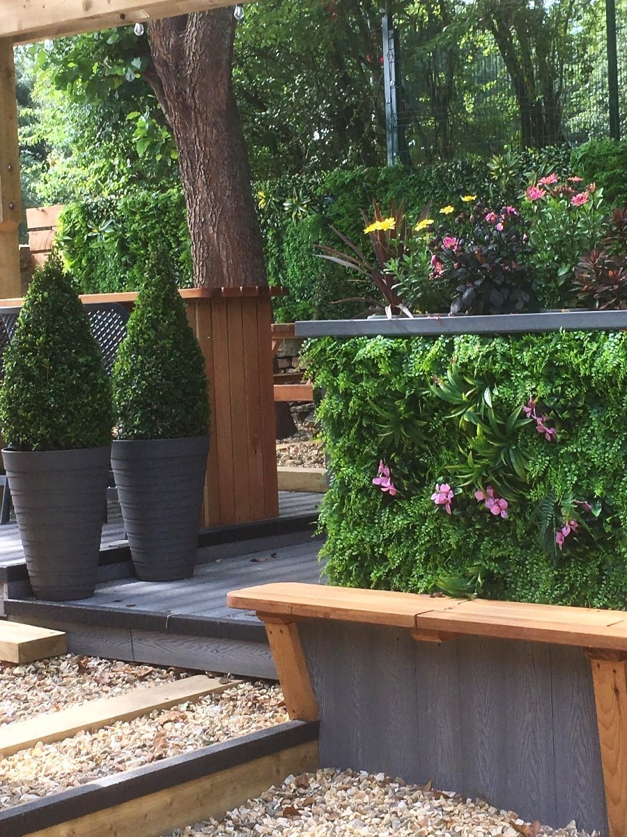 Artificial green wall panel with green foliage and pink flowers on an outdoor wall