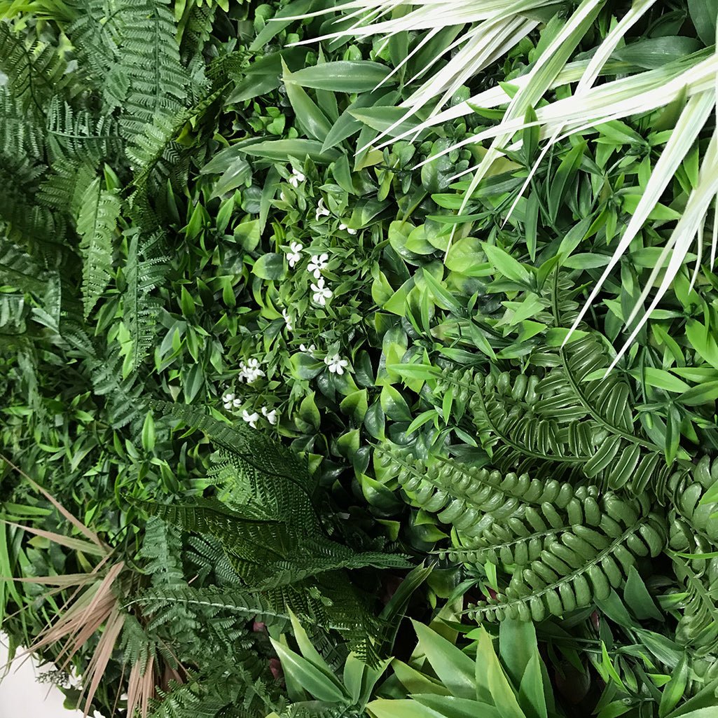 Artificial green foliage wall panel with white flowers and dense mixed-leaf texture