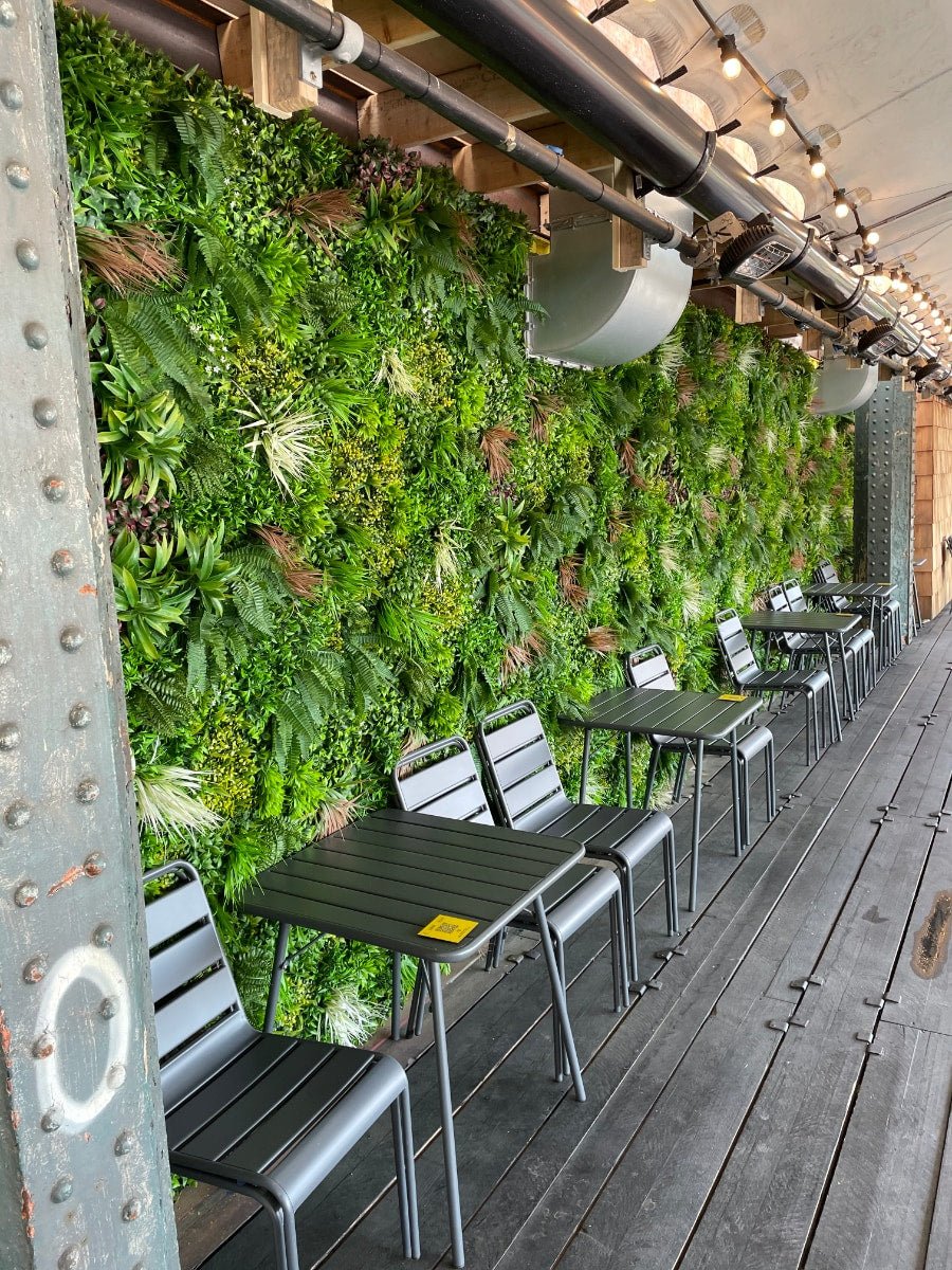 Artificial green foliage wall panel along outdoor wall with dense layered leaves
