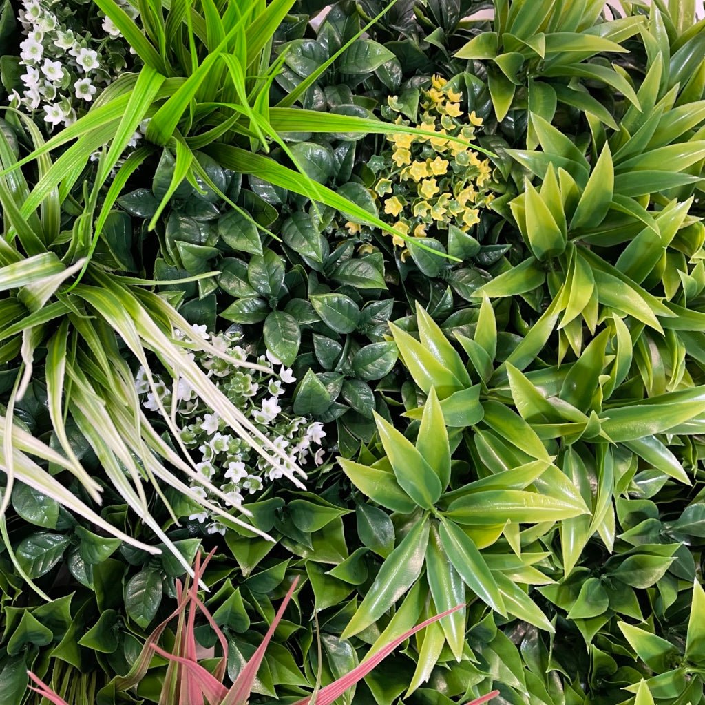 Artificial foliage wall panel close-up with green leaves, small white blossoms, and yellow flowers
