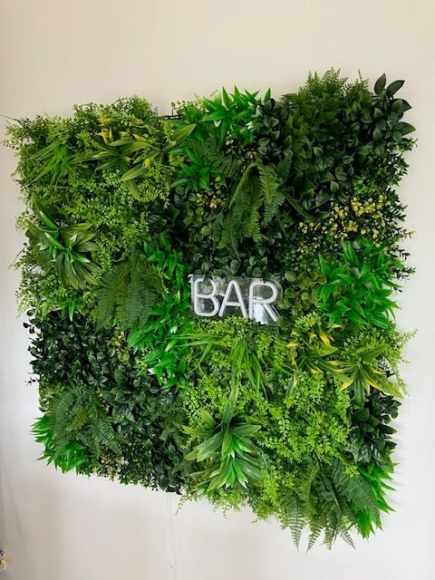 Artificial foliage wall panel with mixed green leaves and a cutout “BAR” sign