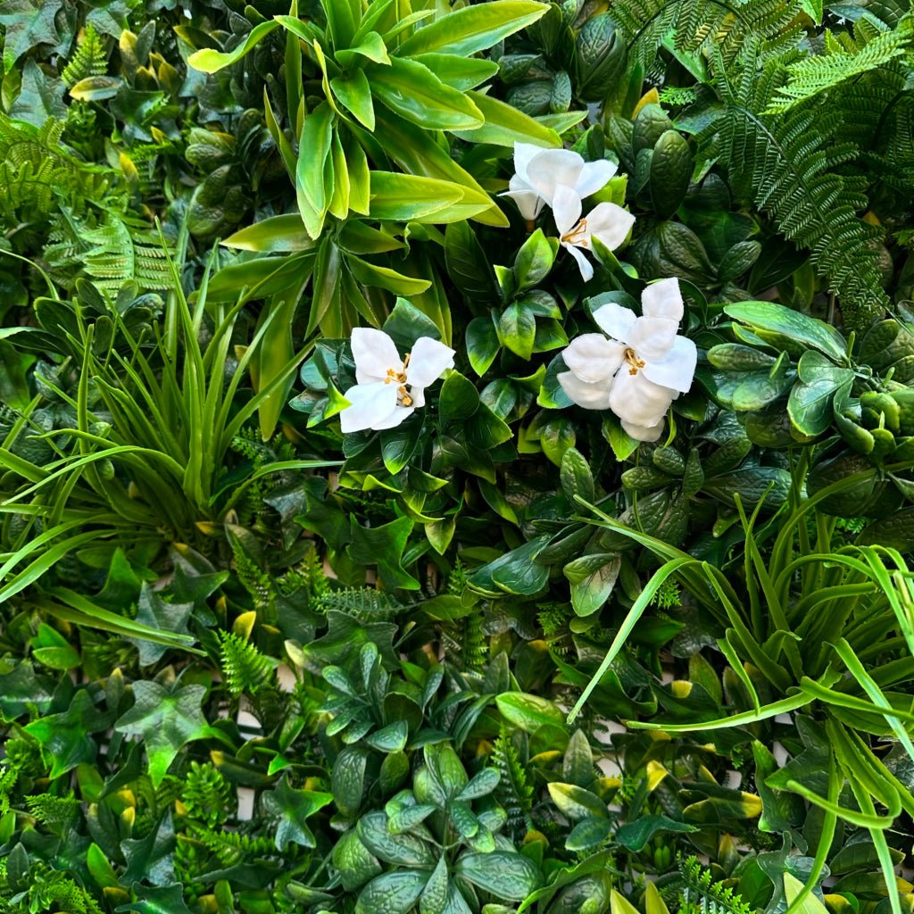 Artificial green foliage wall panel close-up with white orchid-style flowers