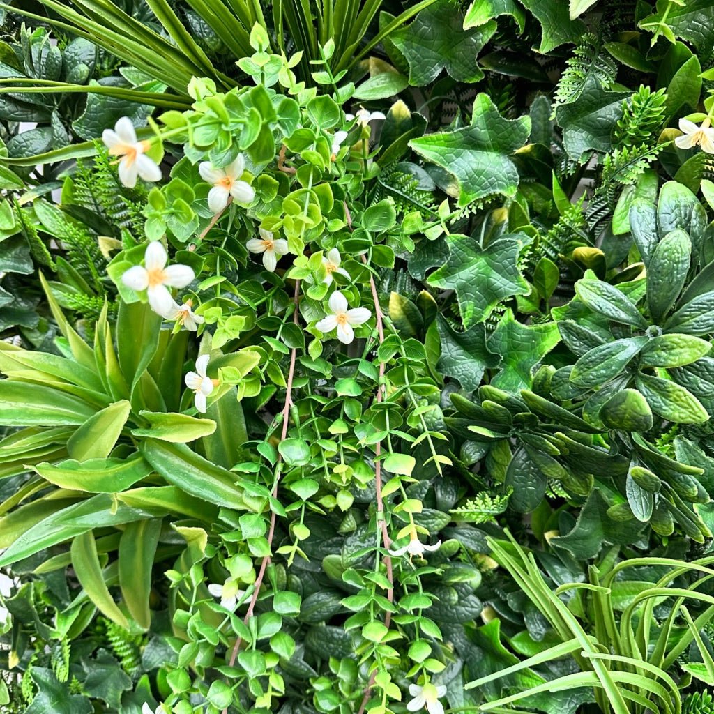Artificial green foliage panel close-up with white dangling flowers and mixed leaf textures