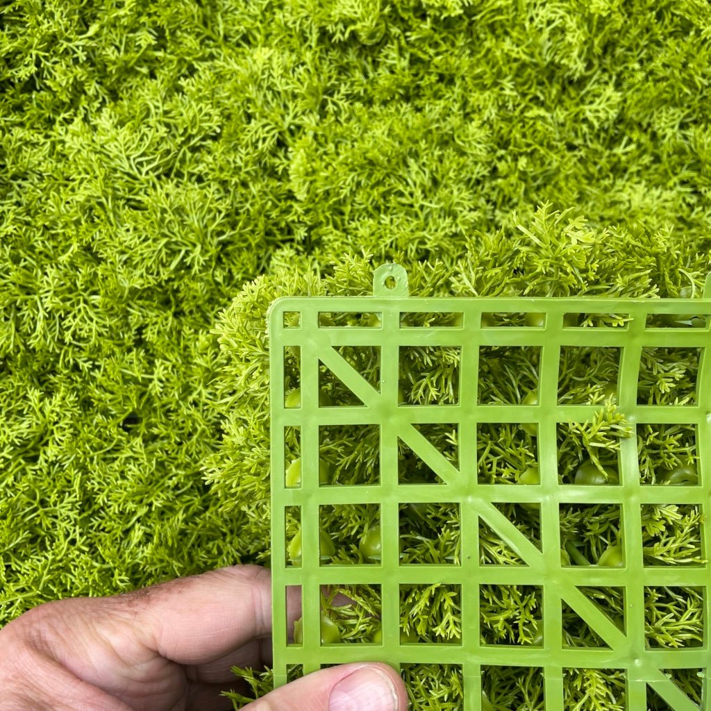 Artificial green moss panel with cutout grid, held by hand